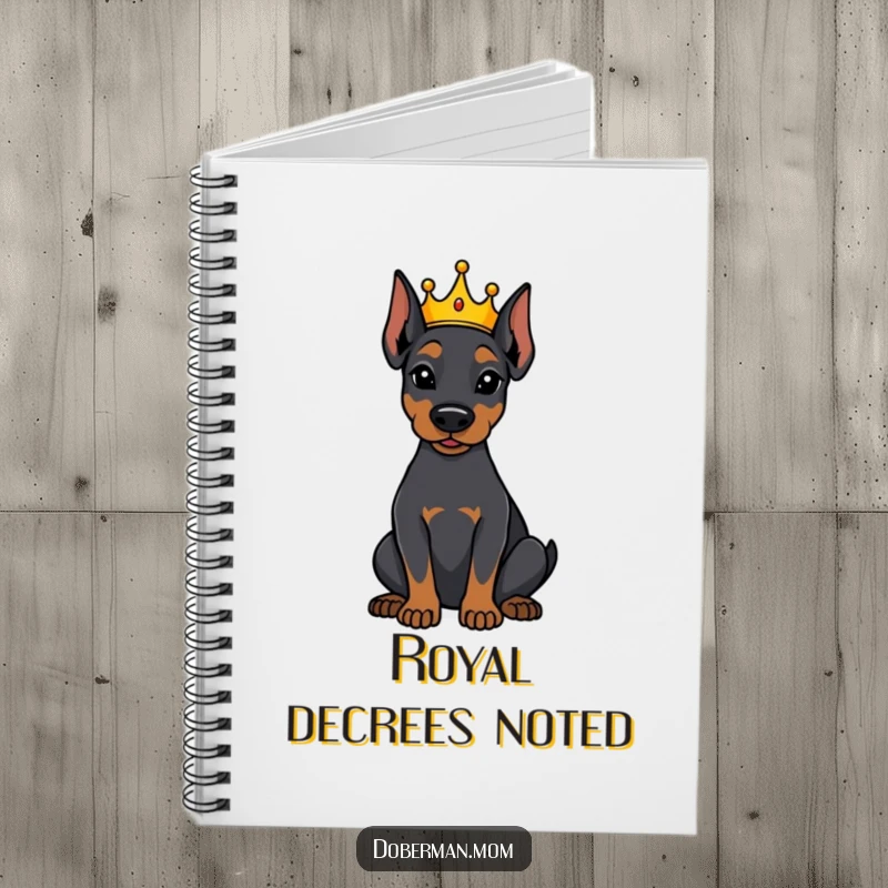 Funny Doberman dog wearing a tiny crown, sitting attentively on a notebook cover, ideal for jotting down regal thoughts.